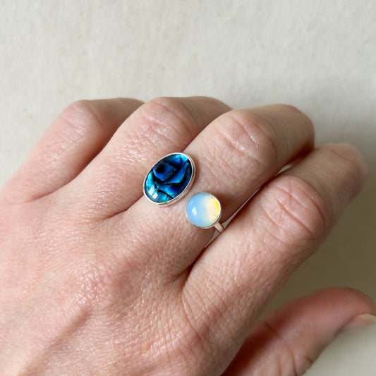 Blue green gemstone ring on persons hand with gray background