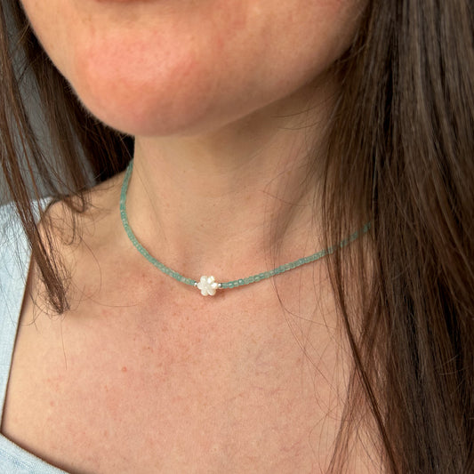 Person wearing a delicate necklace with a small flower pendant.
