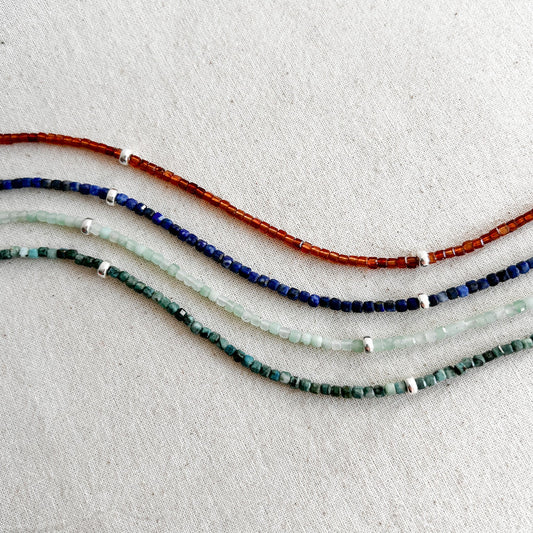 Four beaded necklaces in red, blue, and green on a light gray background