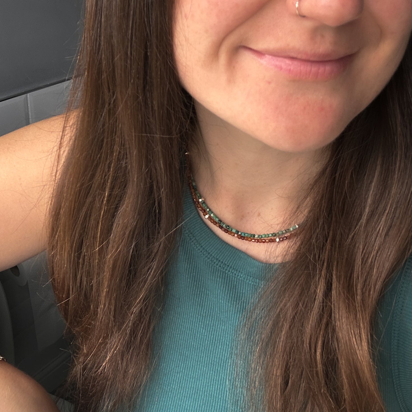 Close-up of a person with long brown hair wearing a green top and beaded necklaces
