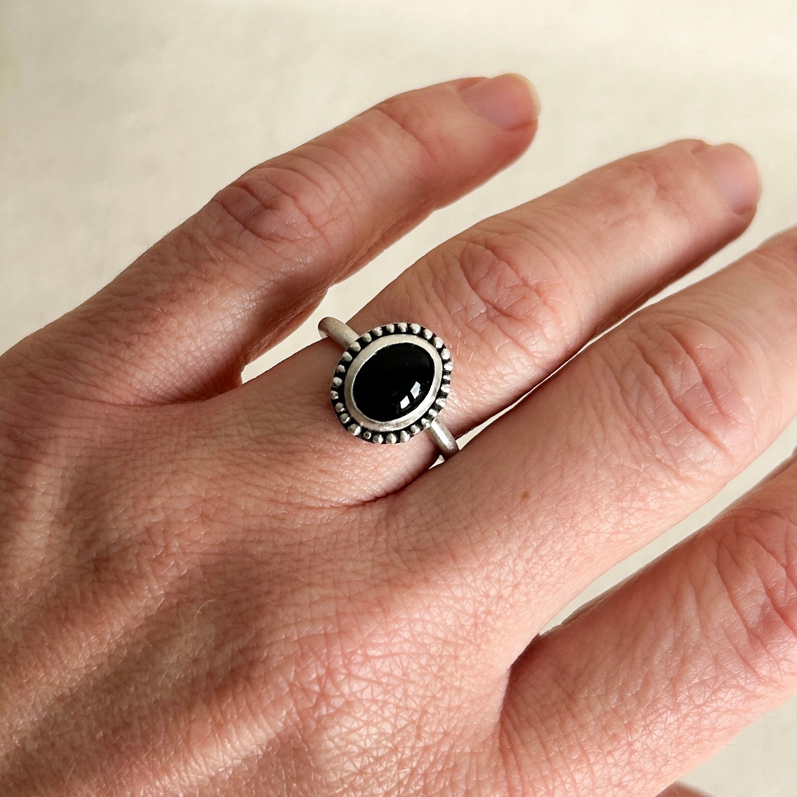 Hand wearing a silver ring with a black gemstone on a neutral background