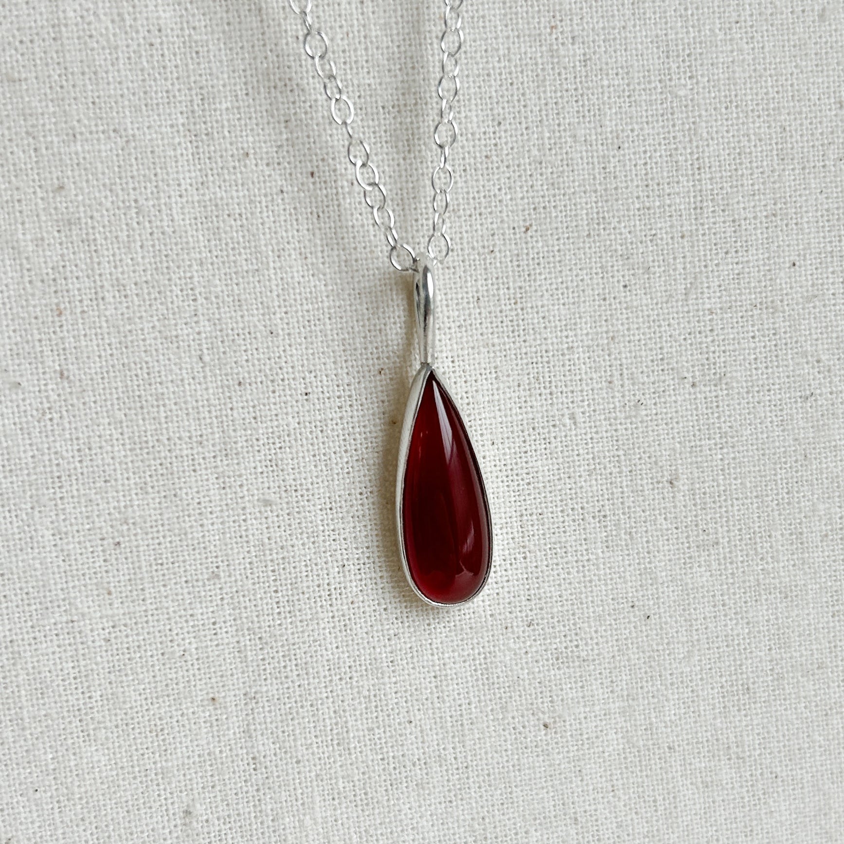 Teardrop-shaped red pendant on a silver chain against a light gray background