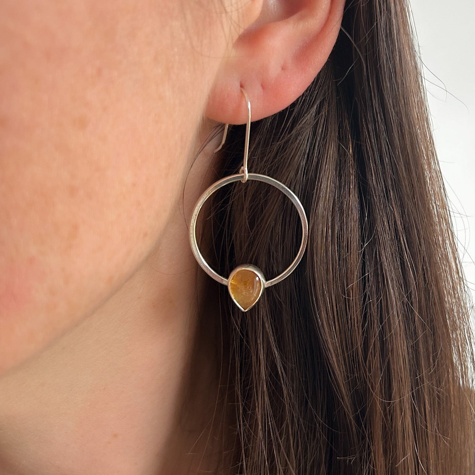 Close-up of a model wearing a silver hoop earring with a citrine gemstone.