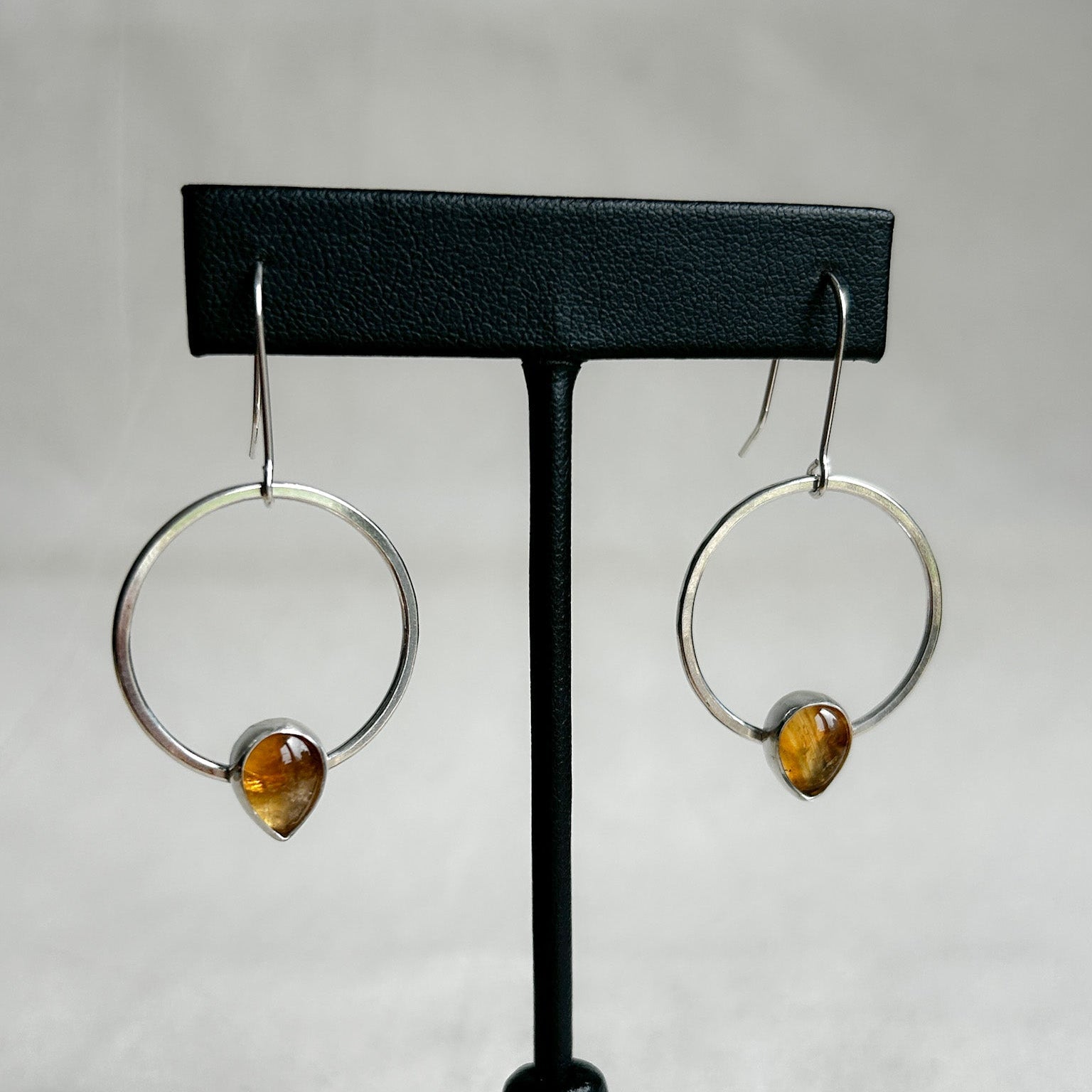 Silver dangle earrings with teardrop shaped citrine gemstones on display stand.