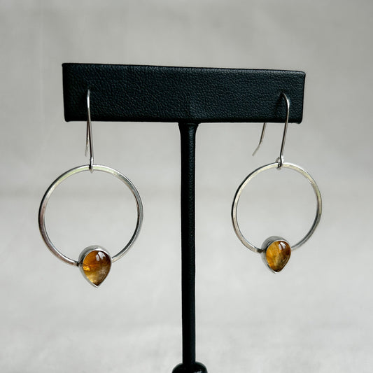 Silver dangle earrings with teardrop shaped citrine gemstones on display stand.