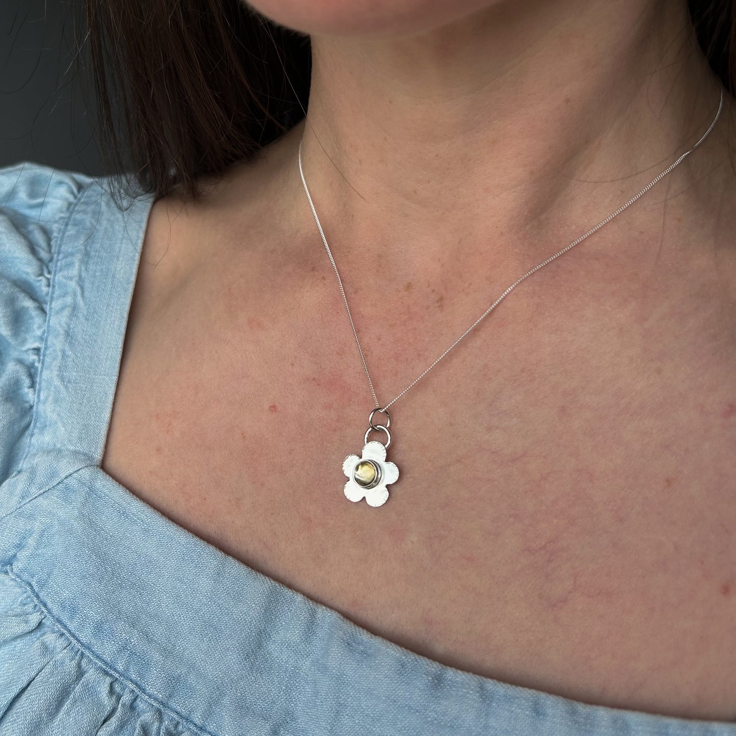 Person wearing a silver necklace with a flower pendant