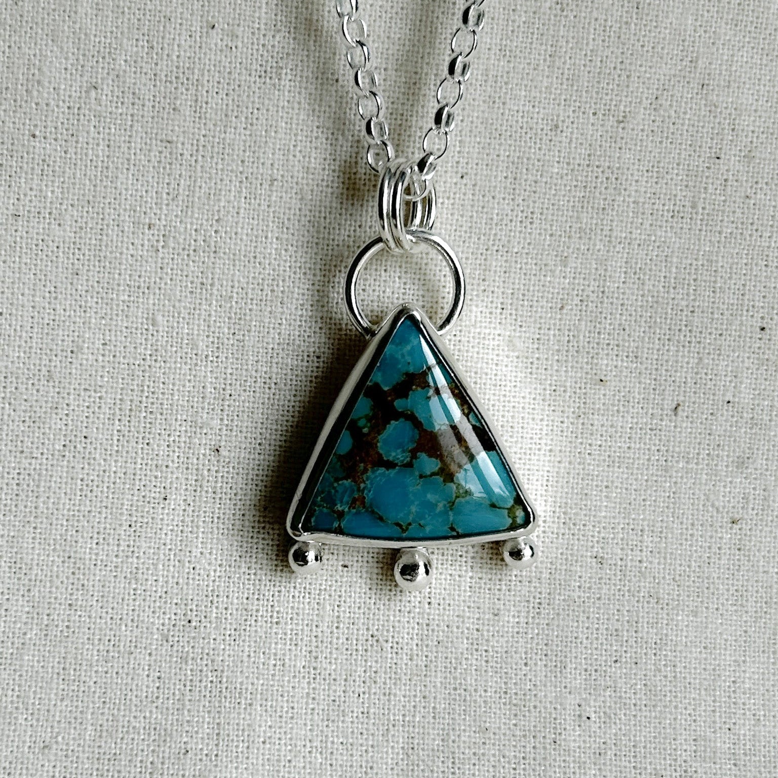 Close up of triangle turquoise pendant on a gray background