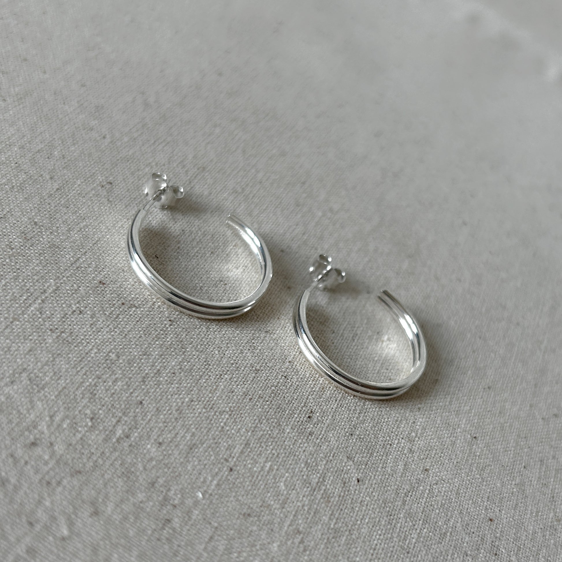 Two small silver ear huggies on a grey background