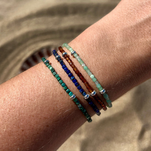 Four gemstone beaded bracelets being modelled on wrist with sand background
