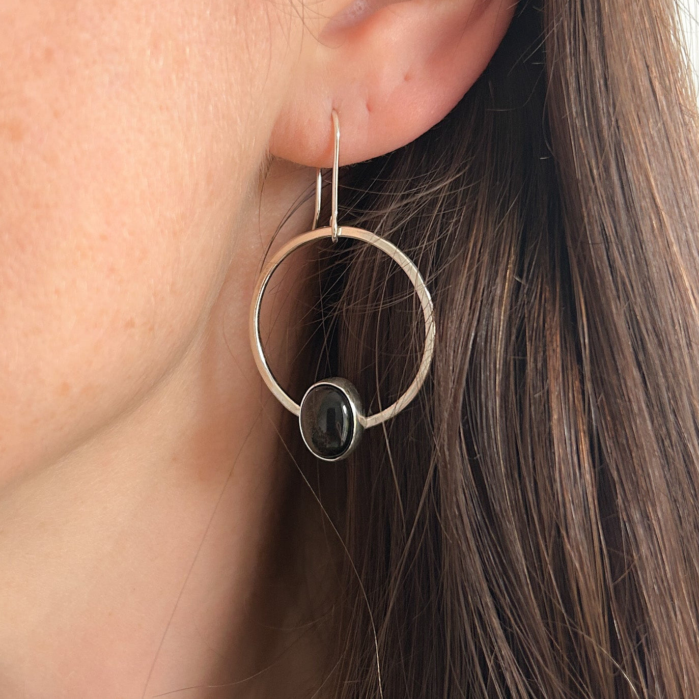 Close up of silver dangle earrings with obsidian gemstone on the bottom