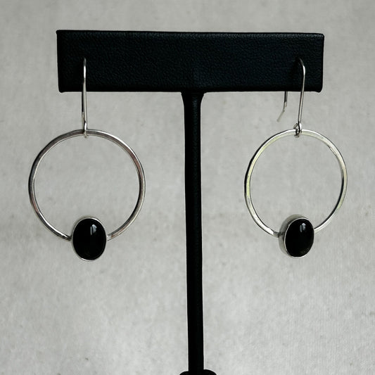 Silver dangle earrings with obsidian gemstones on a black stand against a gray background