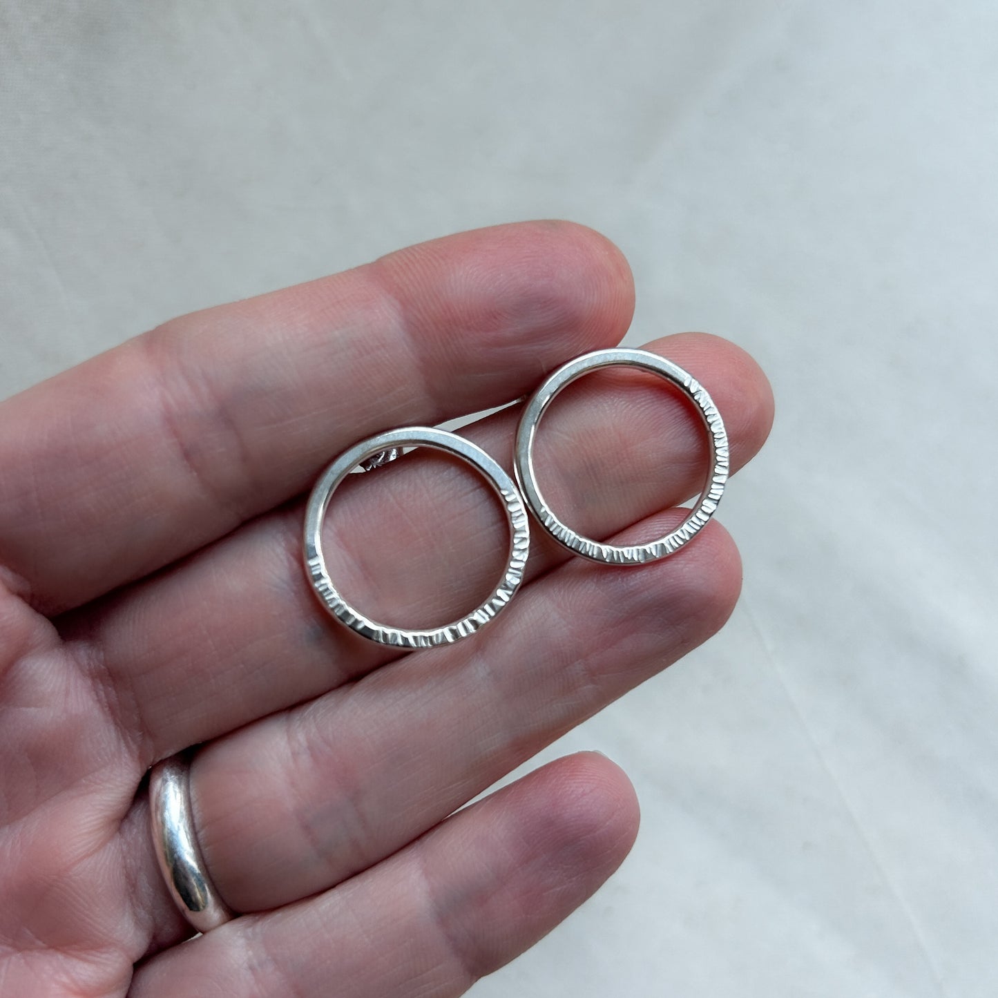 Silver bubble stud earrings shaped like hoops being held by model