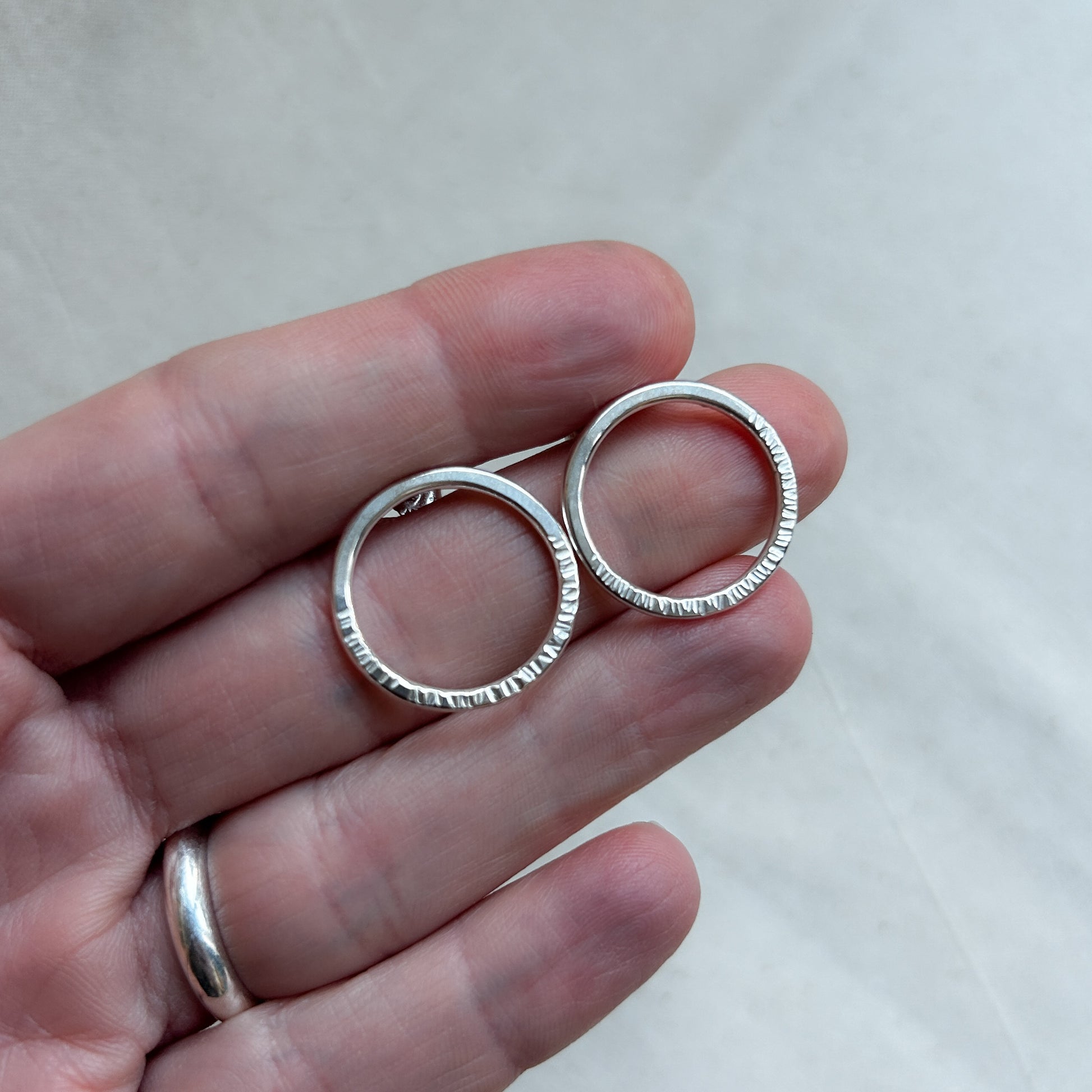 Silver bubble stud earrings shaped like hoops being held by model