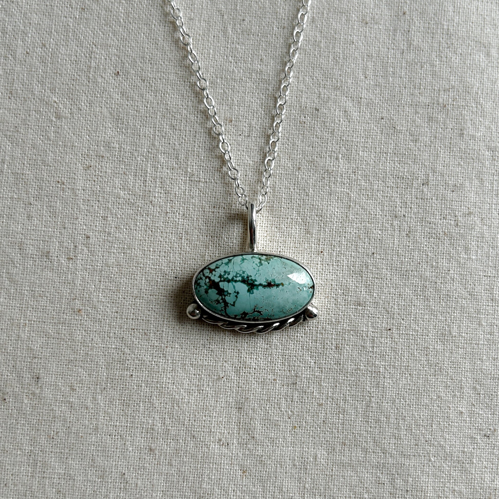 A turquoise pendant necklace on a silver chain, displayed on a neutral background.