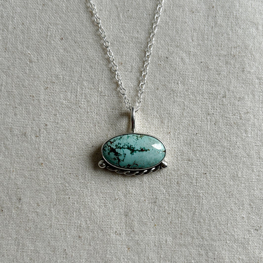A turquoise pendant necklace on a silver chain, displayed on a neutral background.