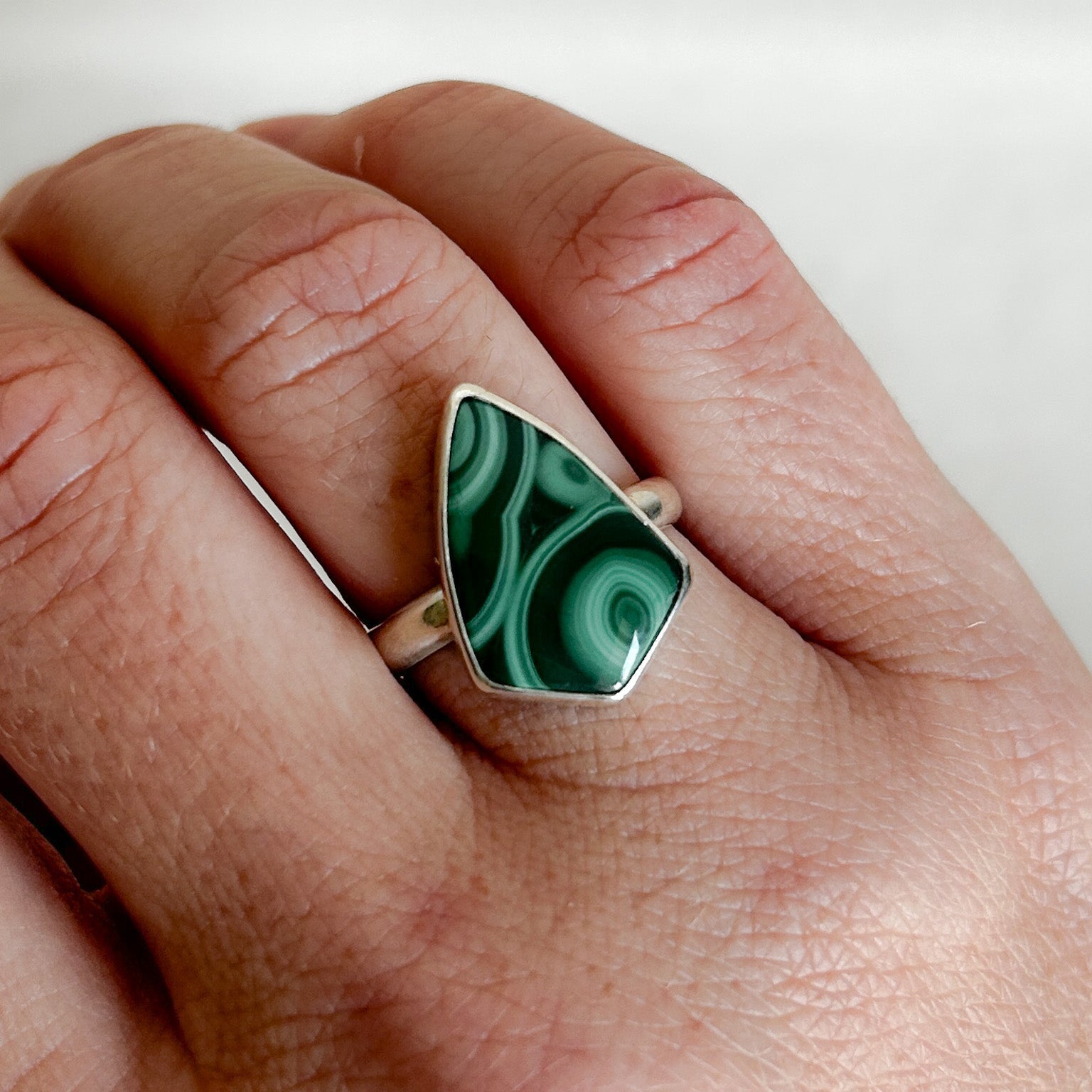 Model wearing a malachite ring with a silver band on a white background