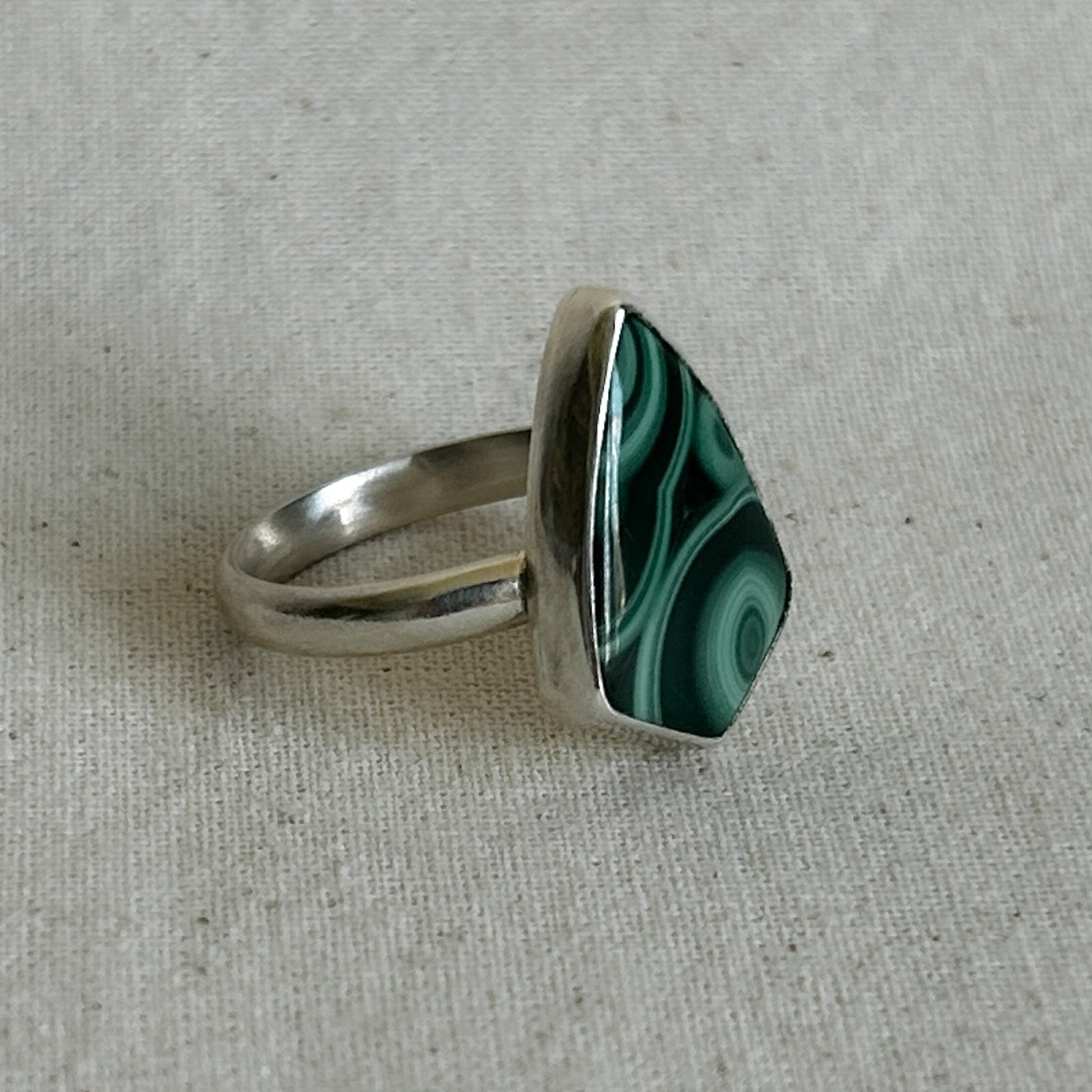 Silver ring with a green and black malachite on a gray fabric background
