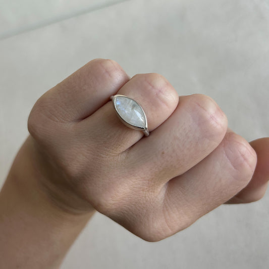 A close-up of a hand wearing a silver ring with a marquise-shaped iridescent white gemstone.