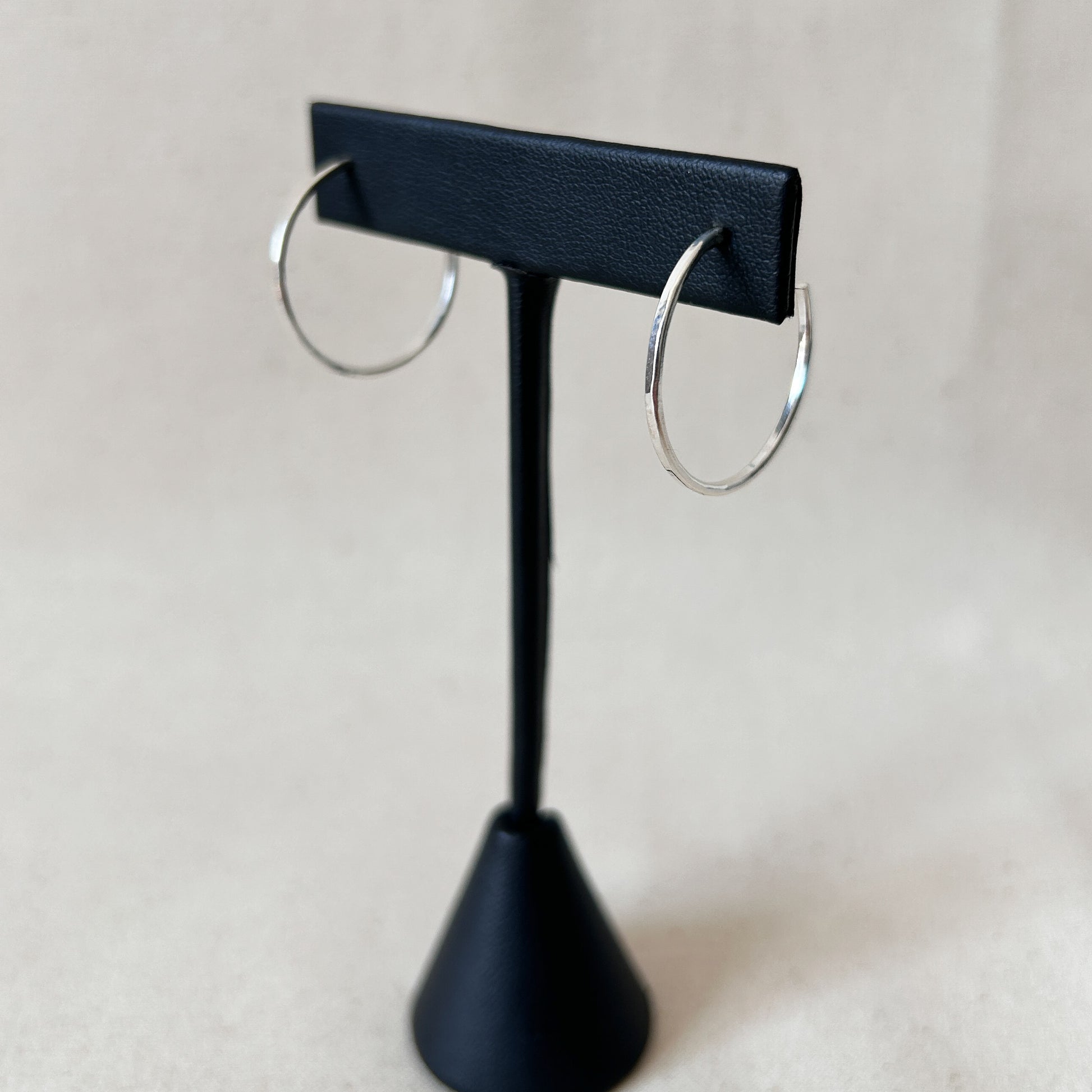 A pair of medium silver hoop earrings displayed on a black stand with a black background.