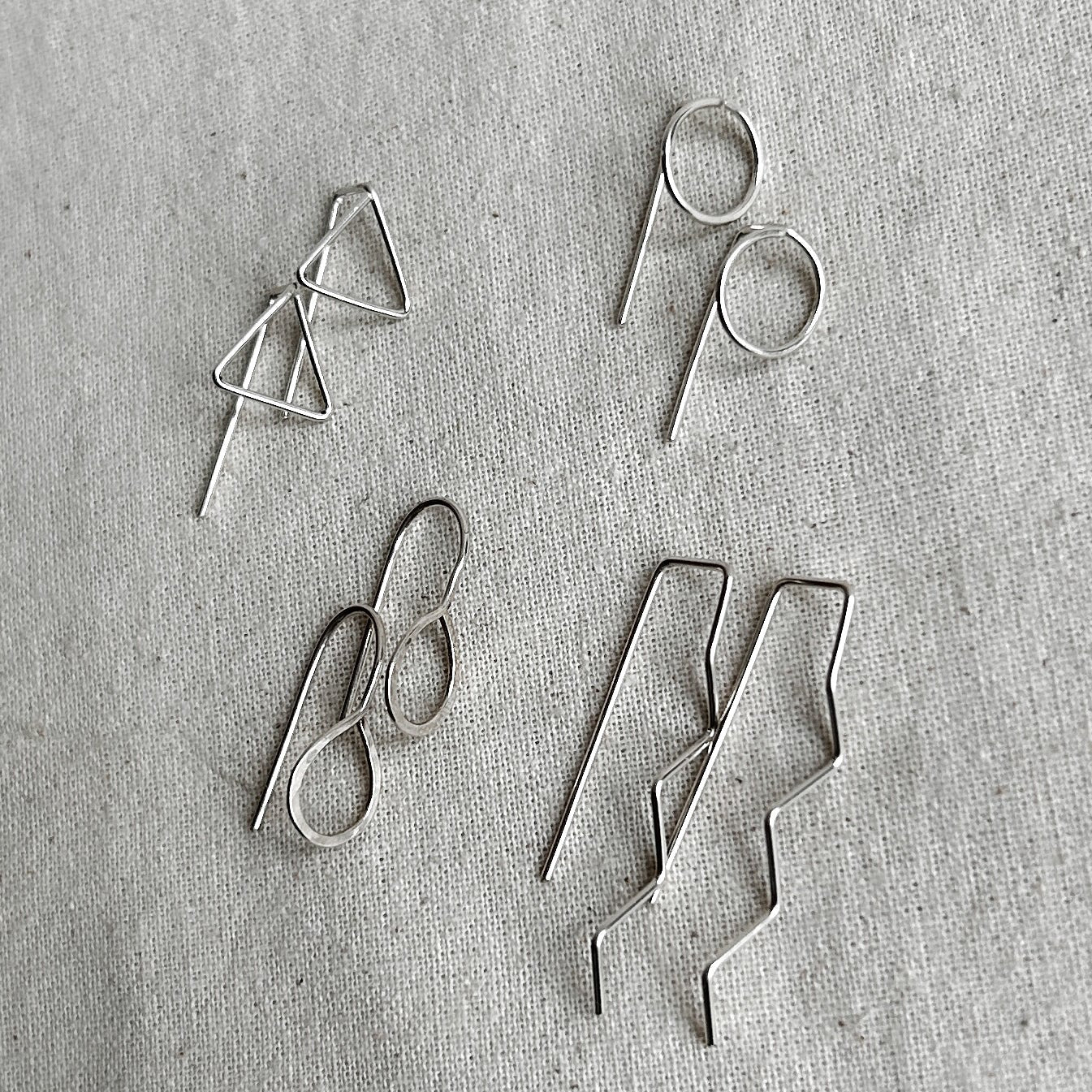 Set of four pairs of silver earrings on a textured gray surface
