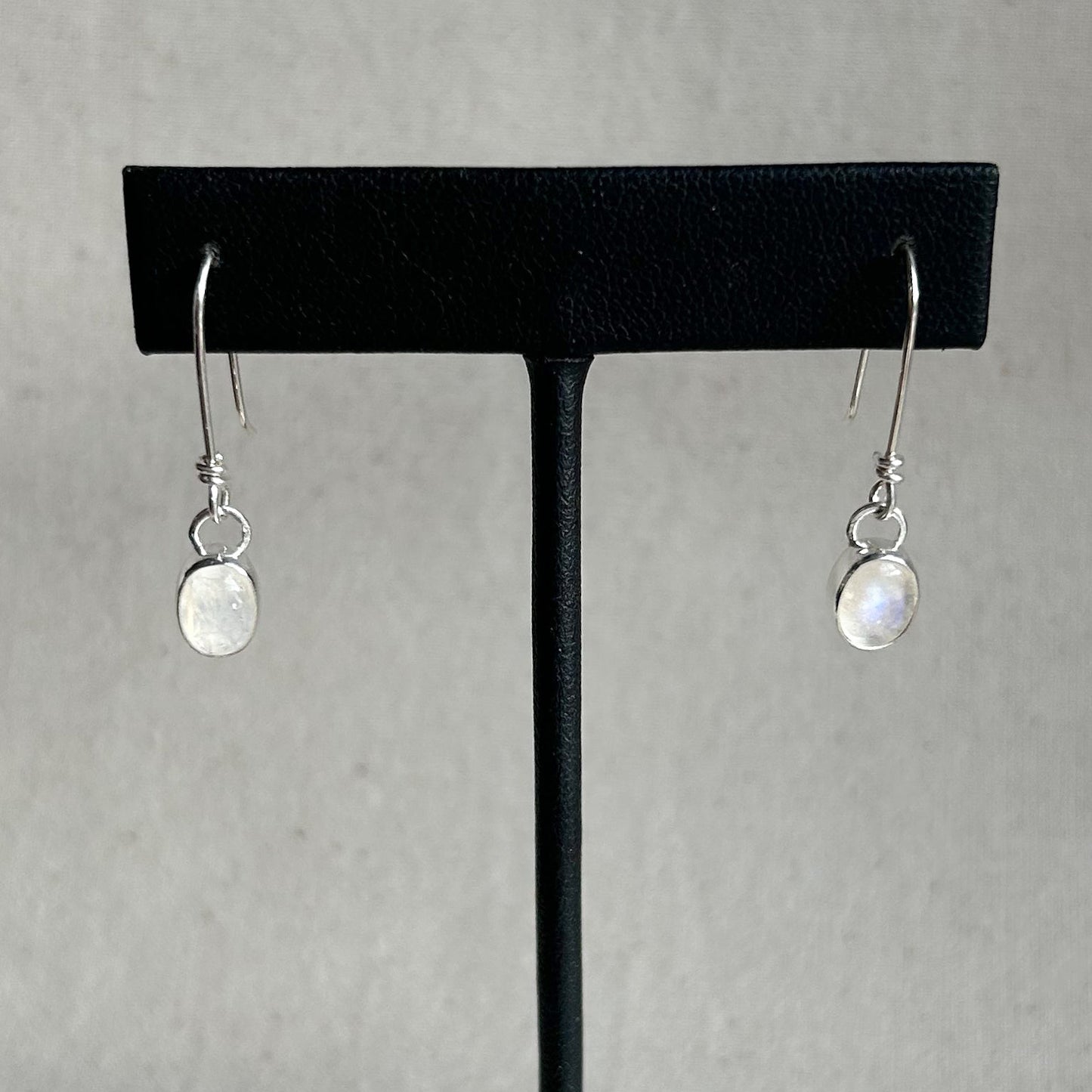 Pair of silver earrings on a black earring stand against a gray background