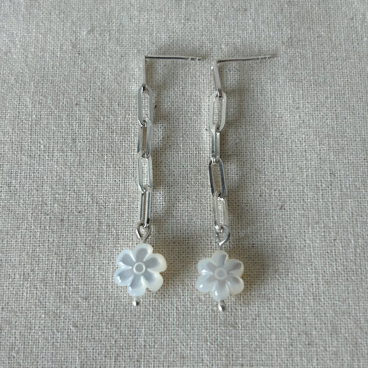 White flower earrings with silver chain laying on a gray background
