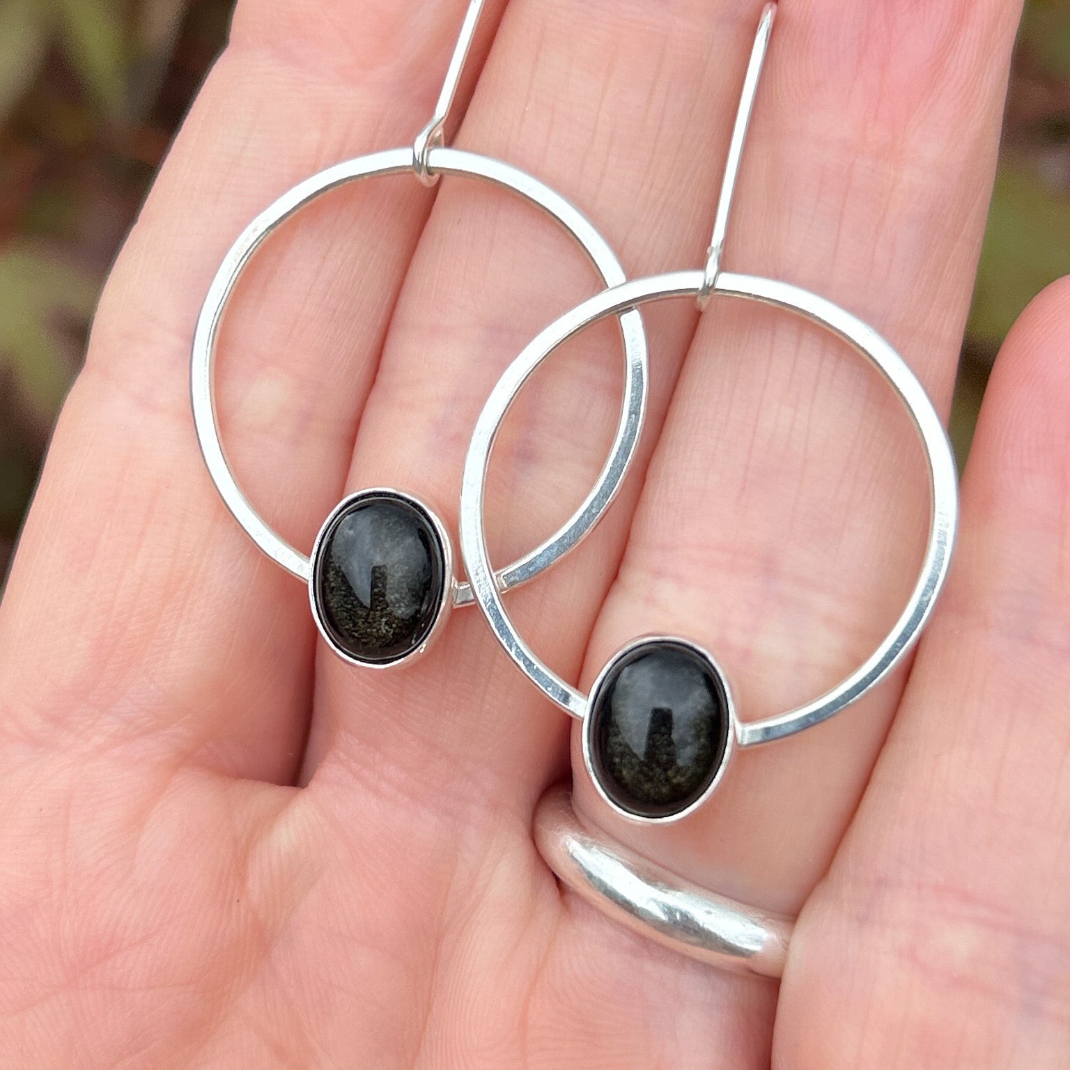 Model holding obsidian earrings  against a blurred natural background
