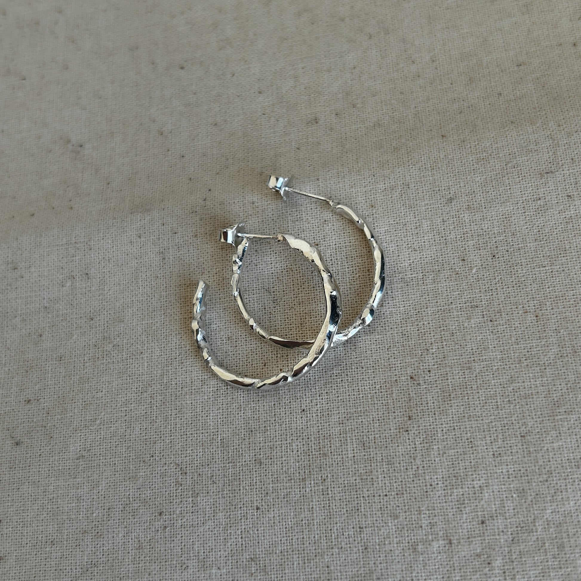 A pair of textured silver hoop earrings laid on a fabric surface.