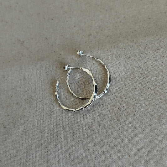 A pair of textured silver hoop earrings laid on a fabric surface.