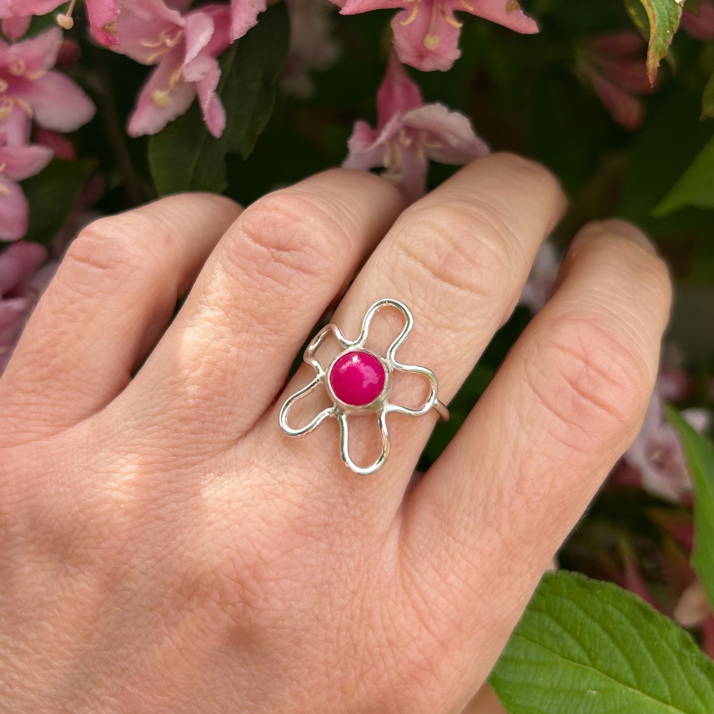 Silver flower shaped ring with pink stone and flower background