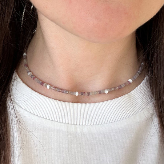 Close-up of a person wearing a delicate beaded necklace with a white top.