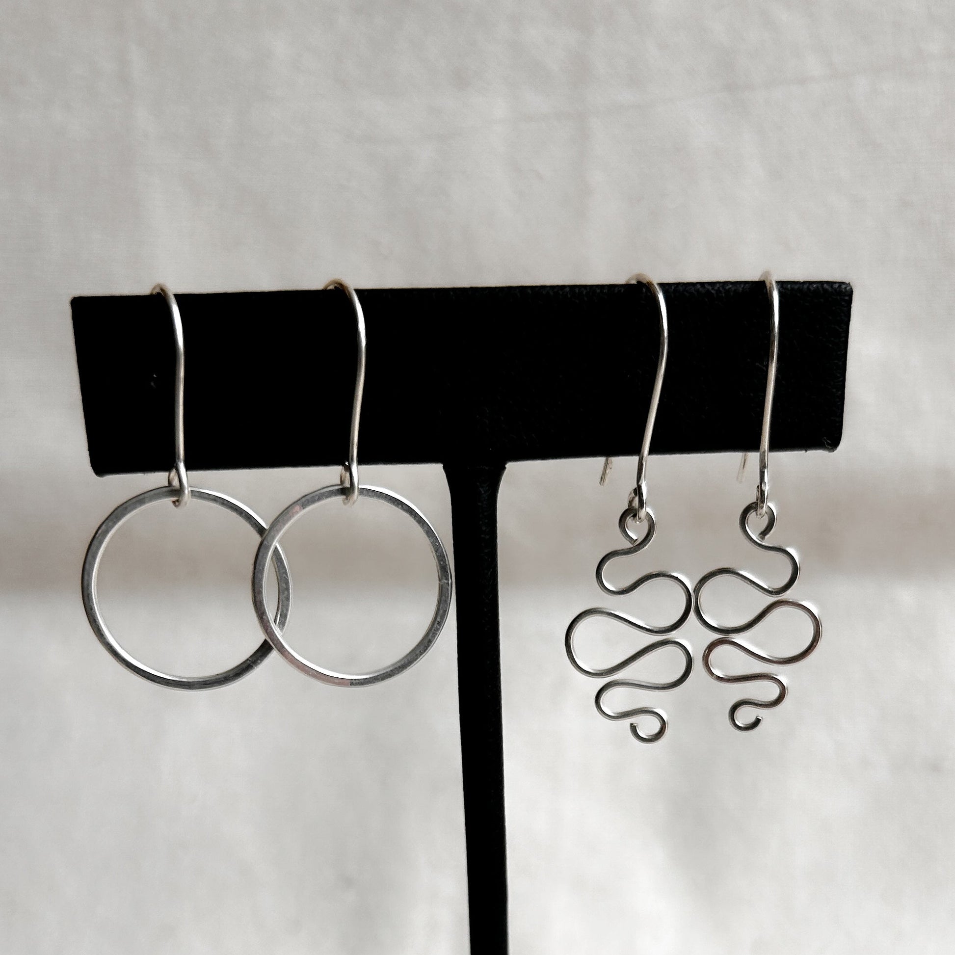 Two pairs of earrings on a black earring stand against a white background