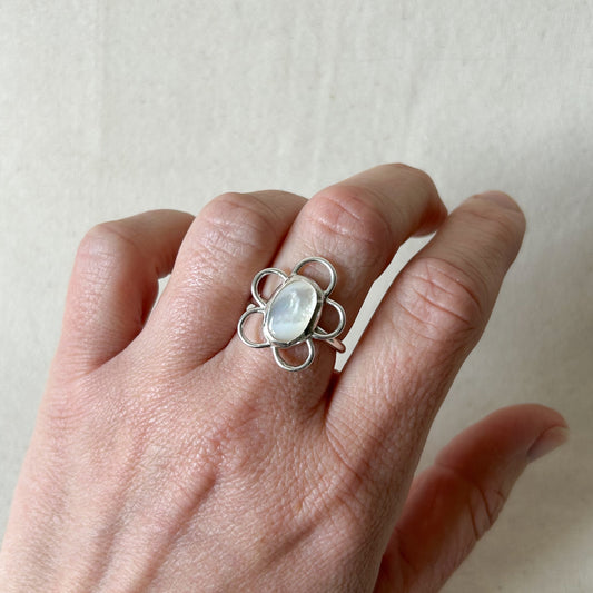 Silver ring with white gemstone on persons hand with gray background