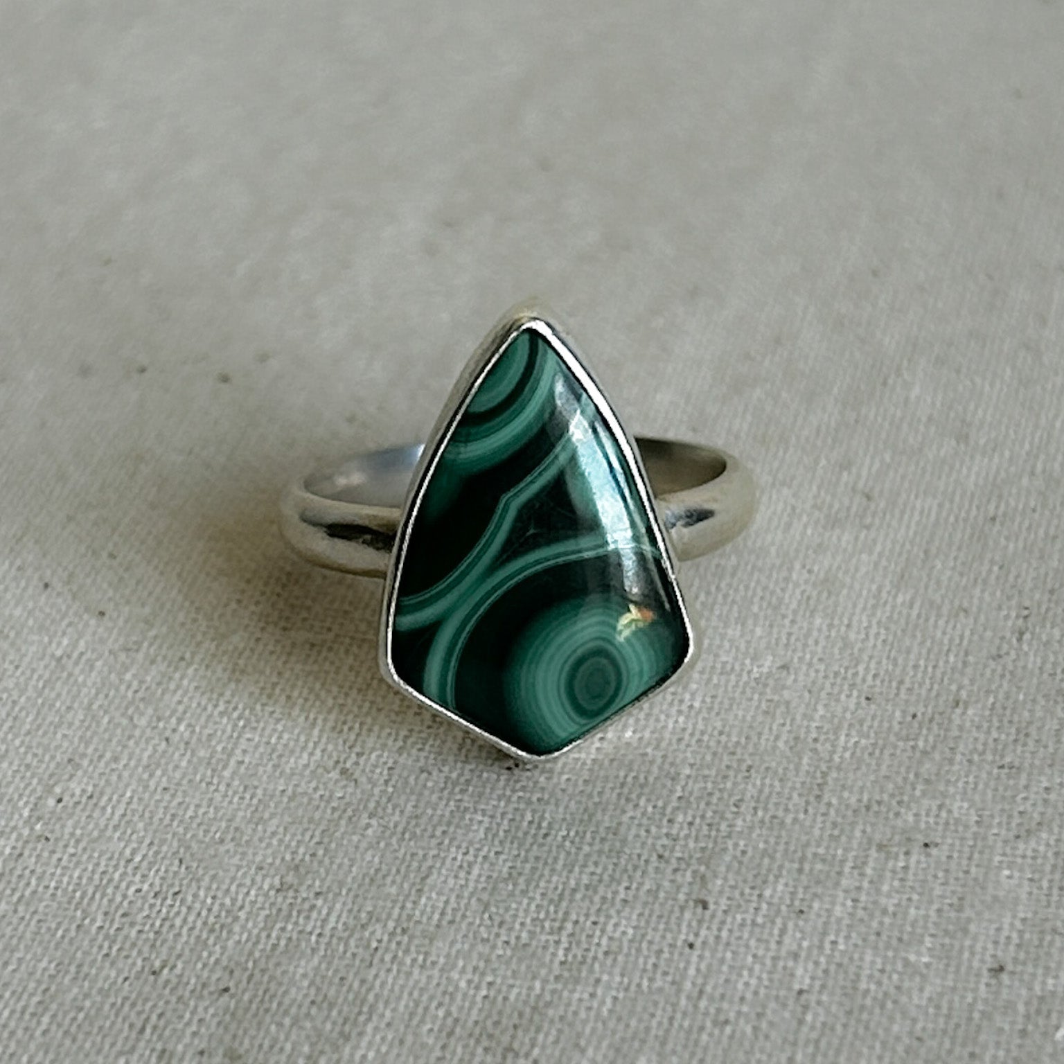Silver and malachite ring with a green triangular stone on a gray background