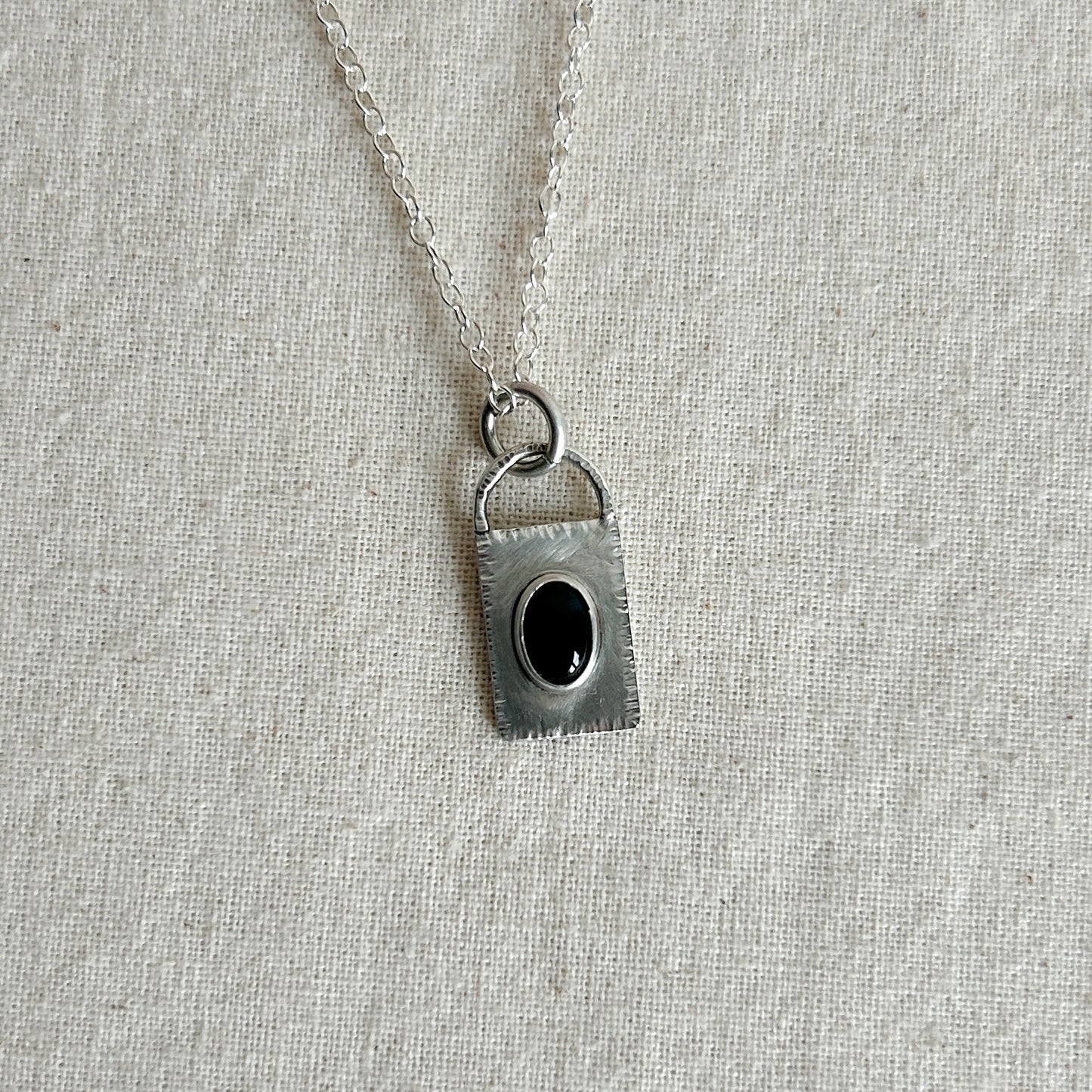 Silver pendant with a black gemstone on a light gray fabric background
