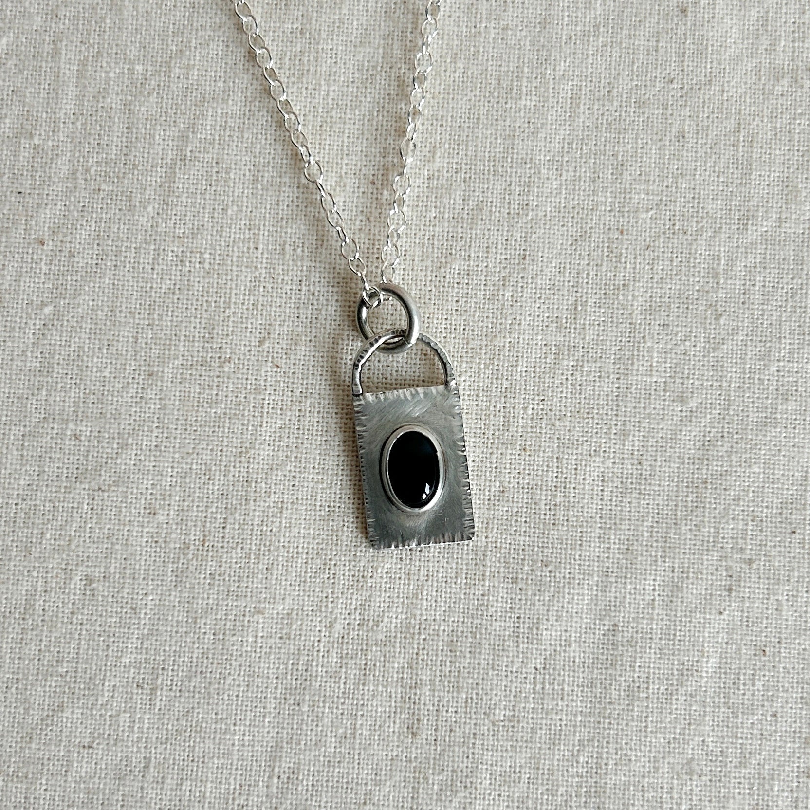 Silver pendant with a black gemstone on a light gray fabric background