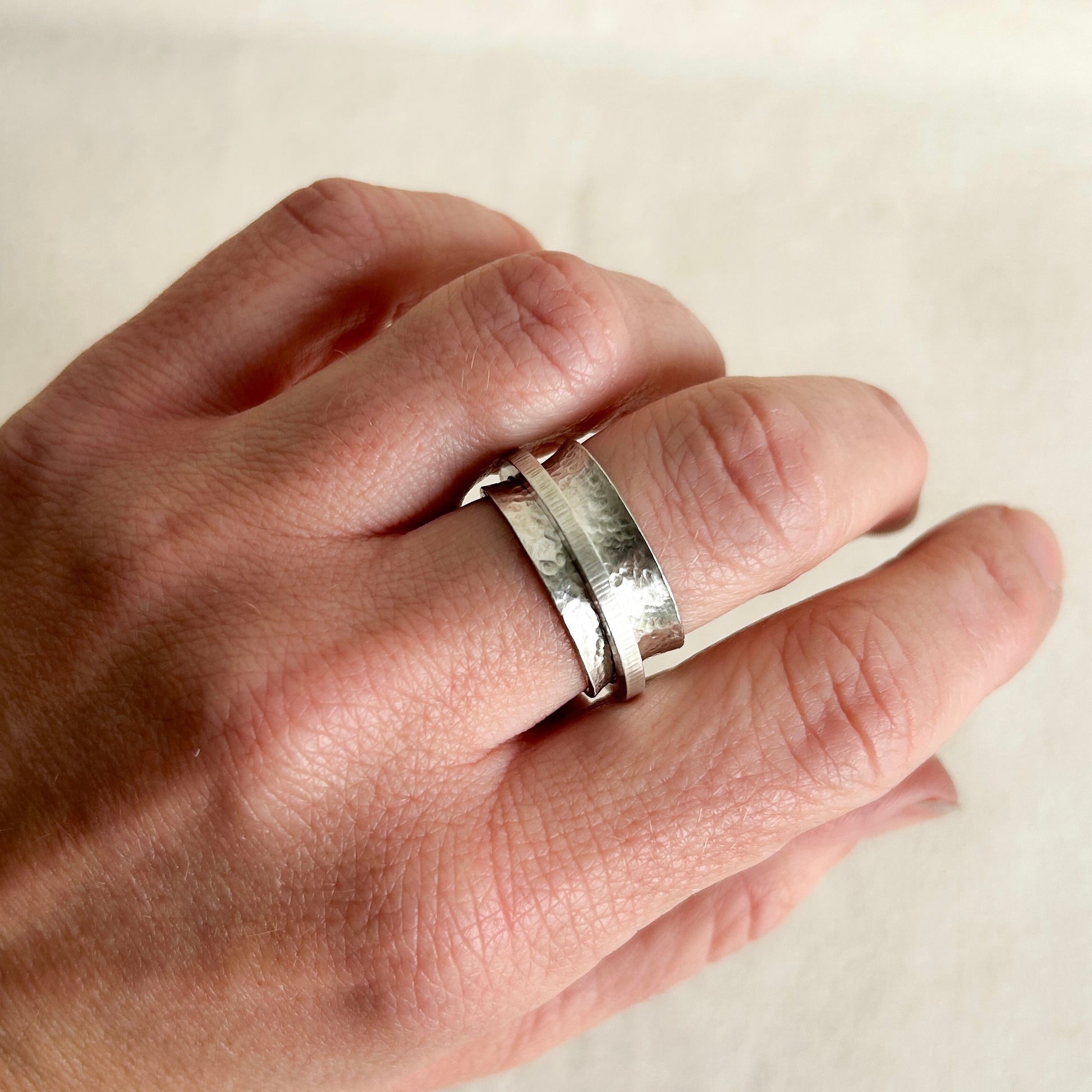 Silver spinner ring on models hand with grey background