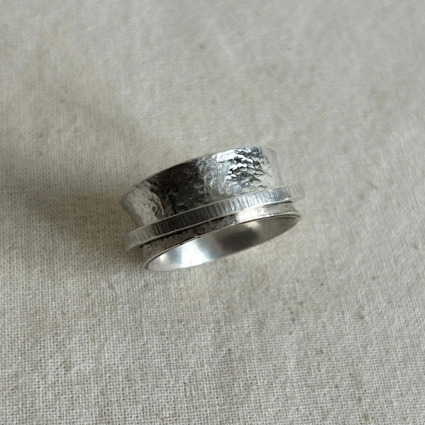 Silver ring with textured design on a light gray fabric background