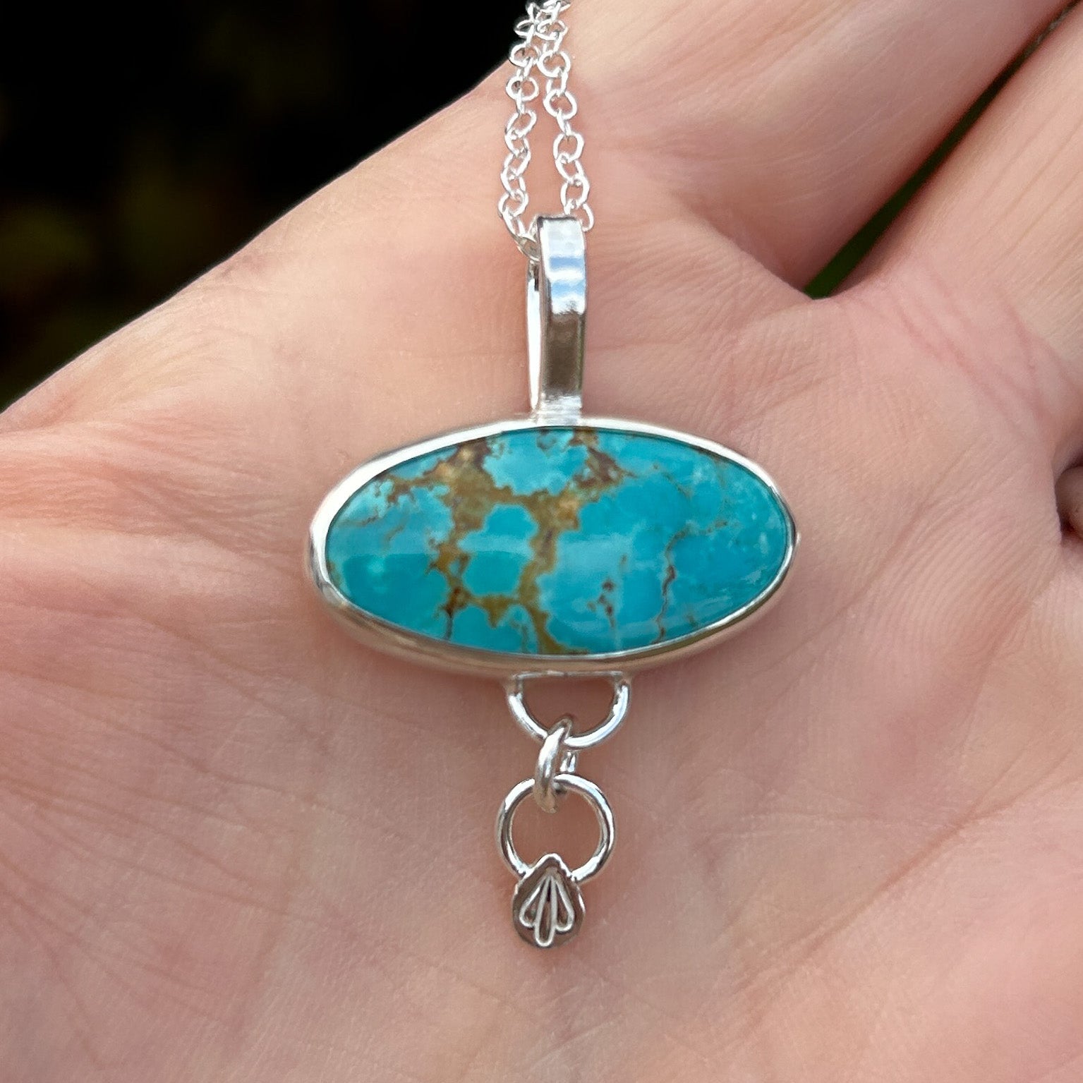 Turquoise pendant necklace held in a hand with a blurred background