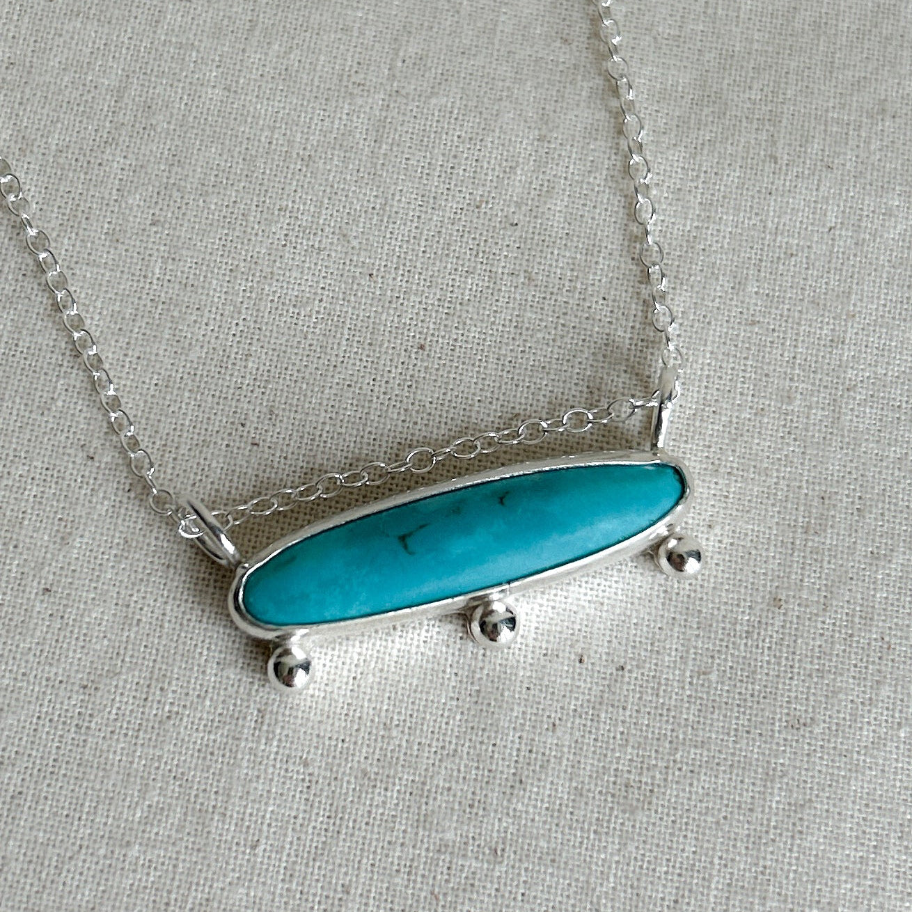Close up of an oblong turquoise gemstone necklace with silver chain