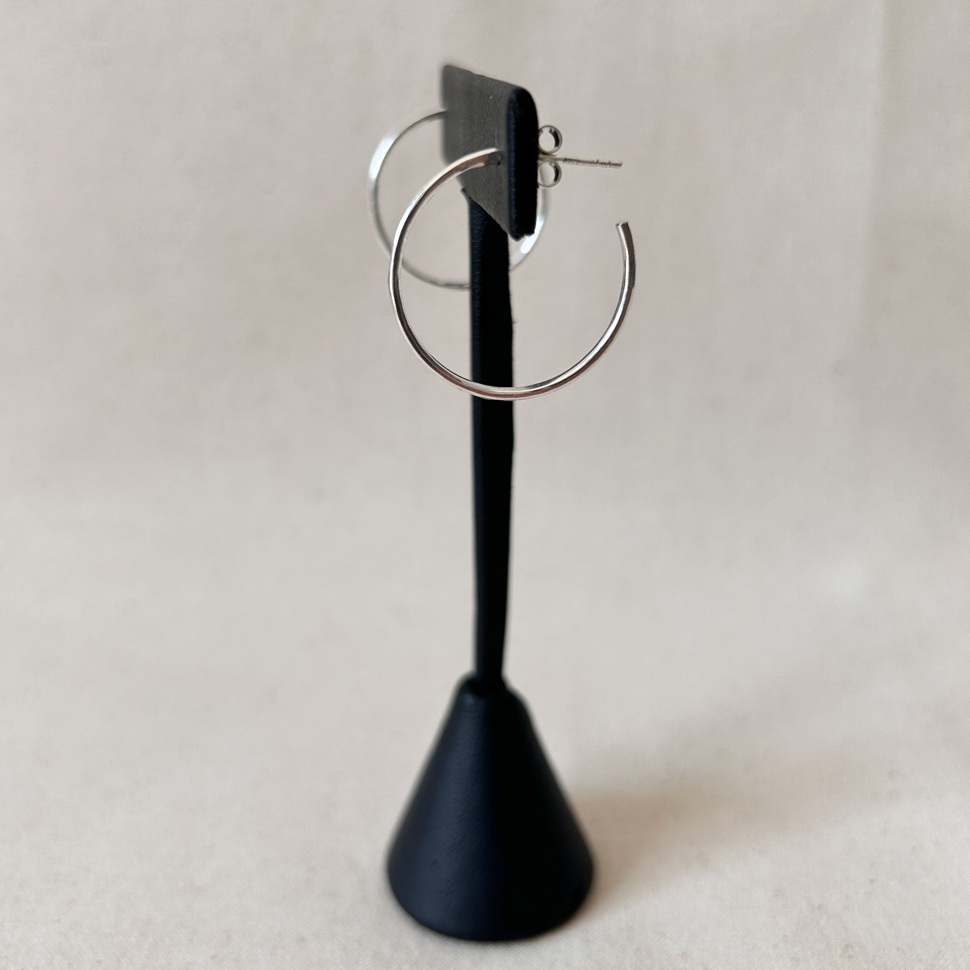 Minimal silver hoop earrings on a black display stand