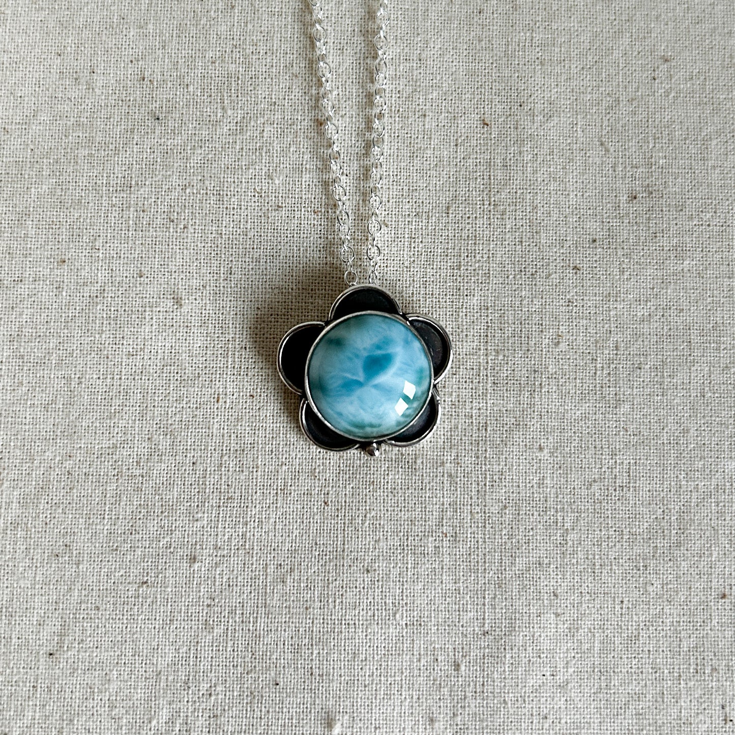 Round larimar gemstone with petal-like design surround, hanging on a silver chain.
