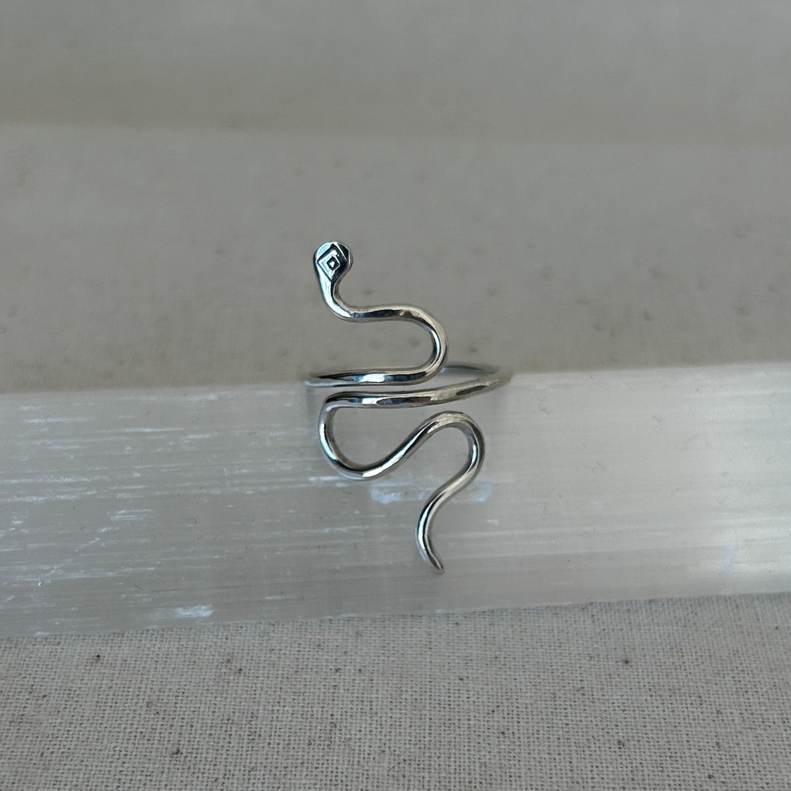 A silver snake ring displayed on a textured surface.