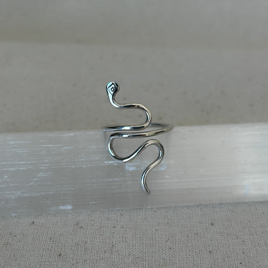 A silver snake ring displayed on a textured surface.
