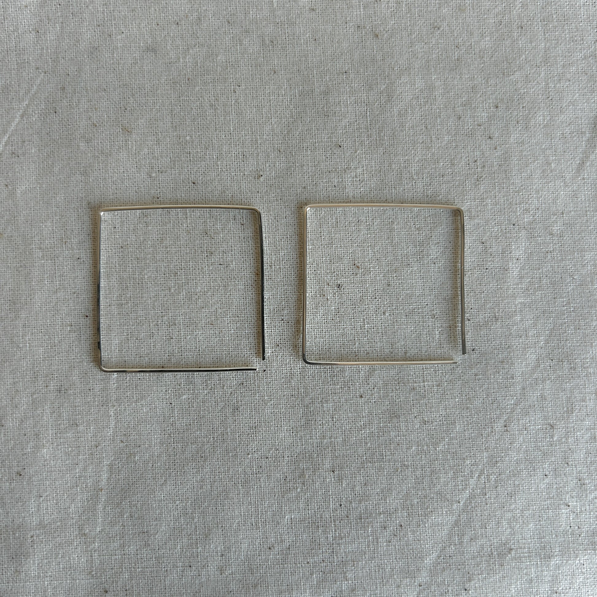 Two silver threader earrings shaped like squares on a grey background