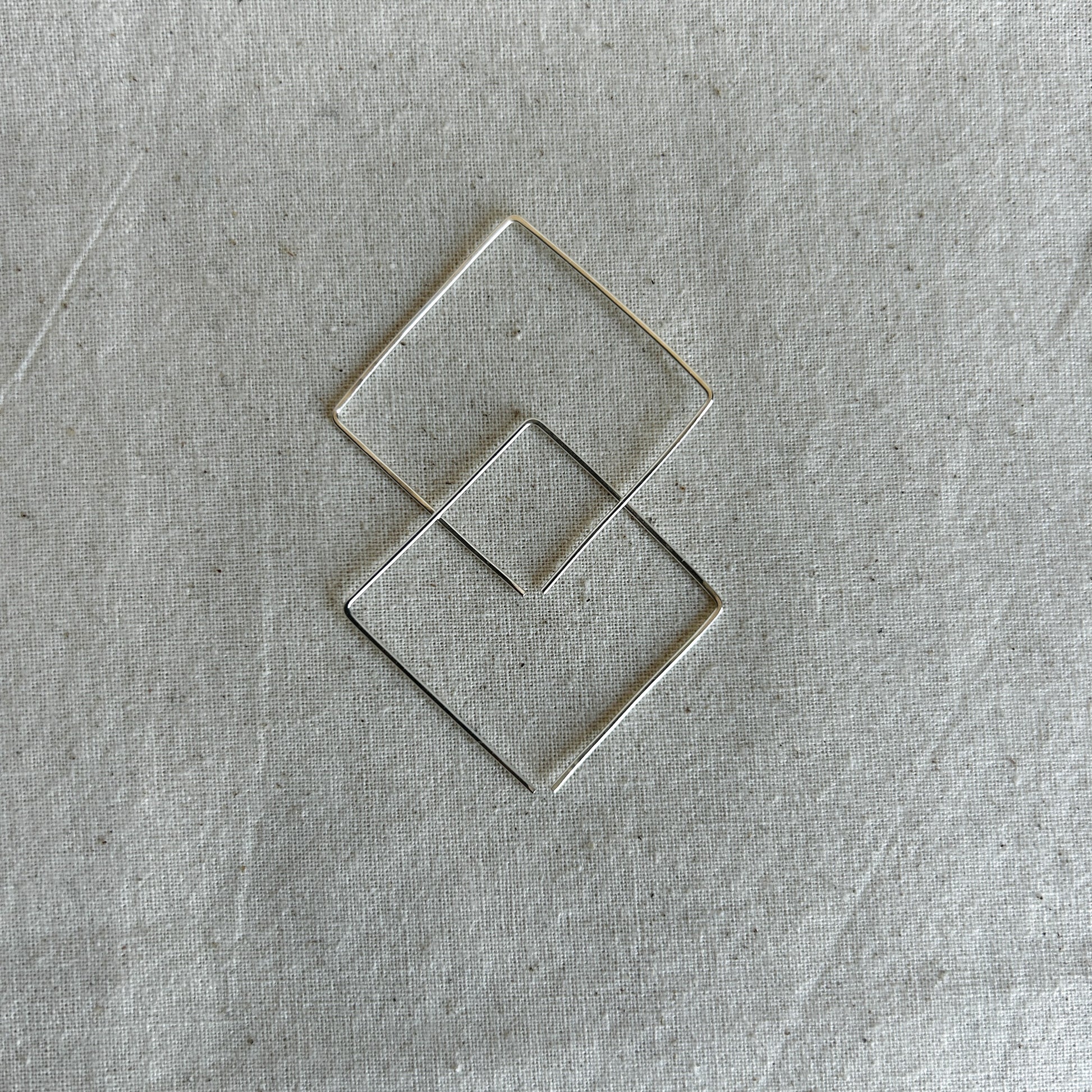 Pair of square silver earrings on a textured gray background