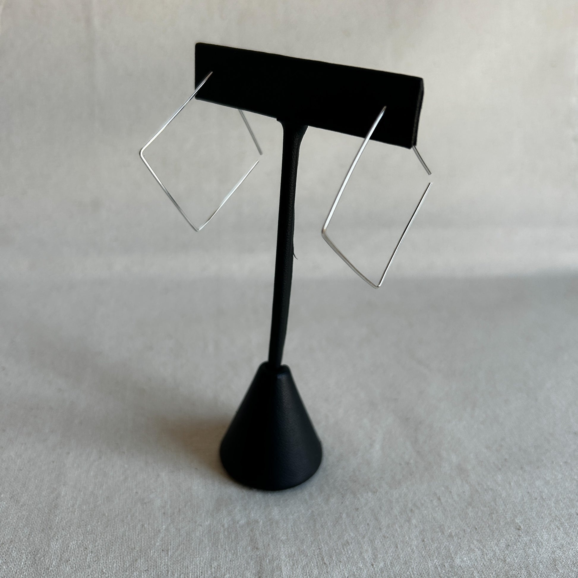 A pair of silver square threader earrings on a black stand against a grey background.