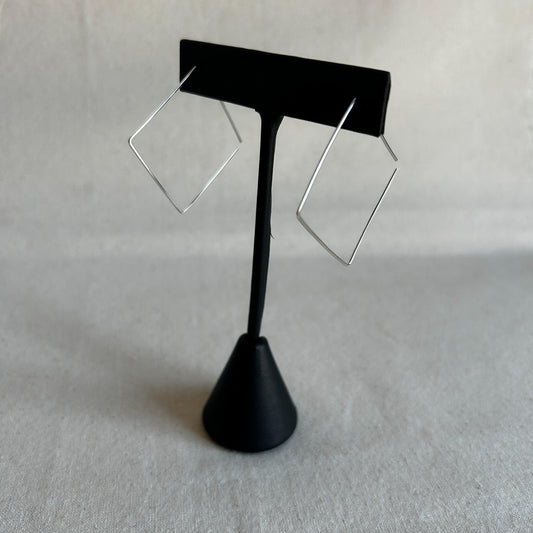 A pair of silver square threader earrings on a black stand against a grey background.