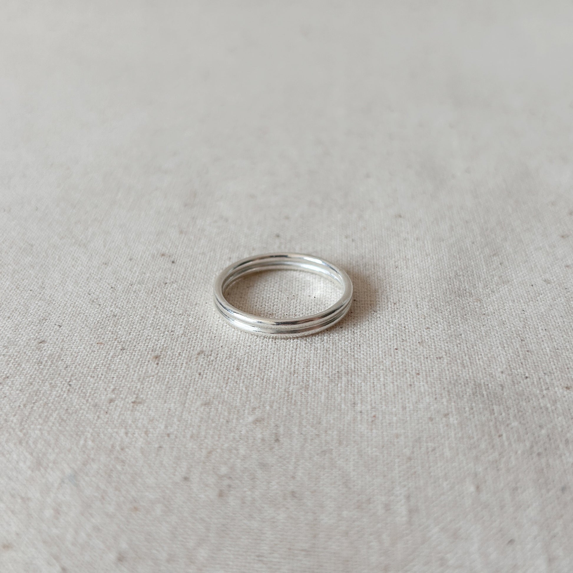 A silver double-band stacking ring on a textured light background.