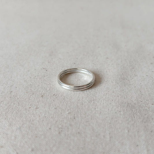A silver double-band stacking ring on a textured light background.